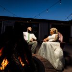Bride and groom sitting by a firepit under string lights at their wedding reception 