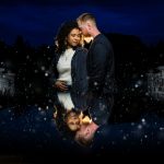 Engaged couple standing close at night with snow effect and artistic reflection in water