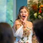 Bride reacting with joyful surprise during a wedding speech or moment.