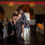Wedding party member giving two guests a piggyback ride during the reception entrance.