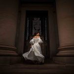 Bride twirls up stone steps in dramatic lighting between large columns at the Philadelphia Museum of Art