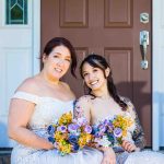 LGBTQ brides sitting together on a front porch in wedding dresses, smiling and holding colorful floral bouquets